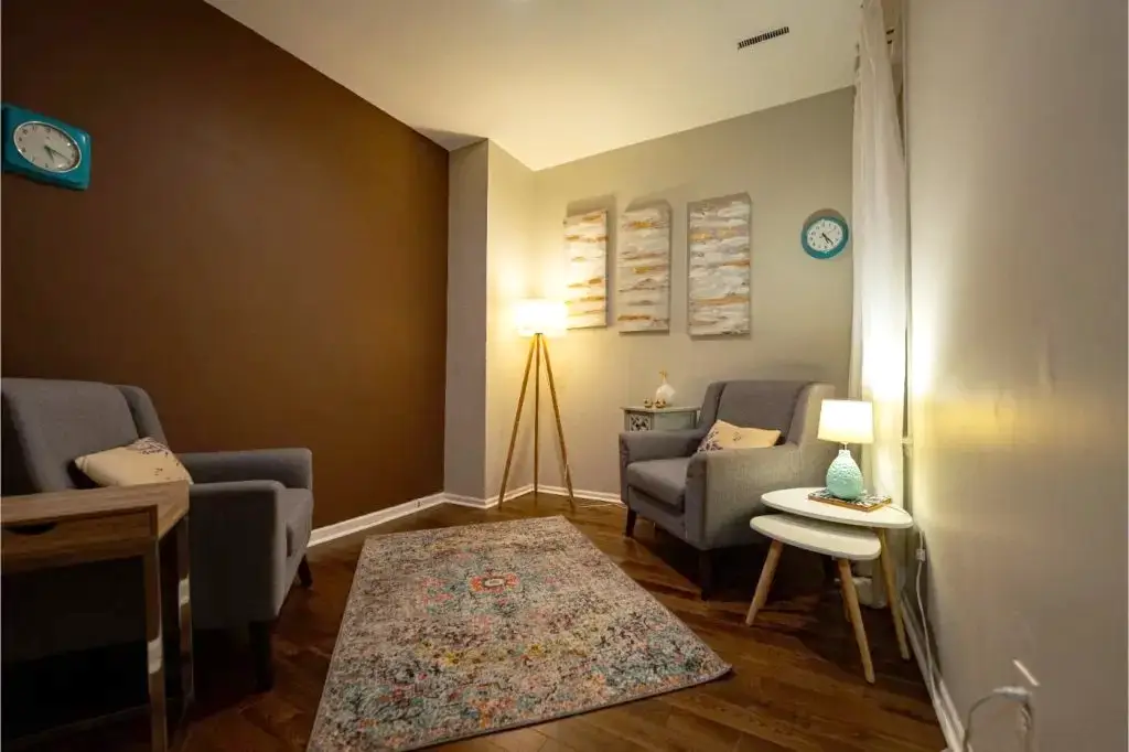 Cozy psychotherapy room with gray armchairs, warm lighting, and a patterned rug.