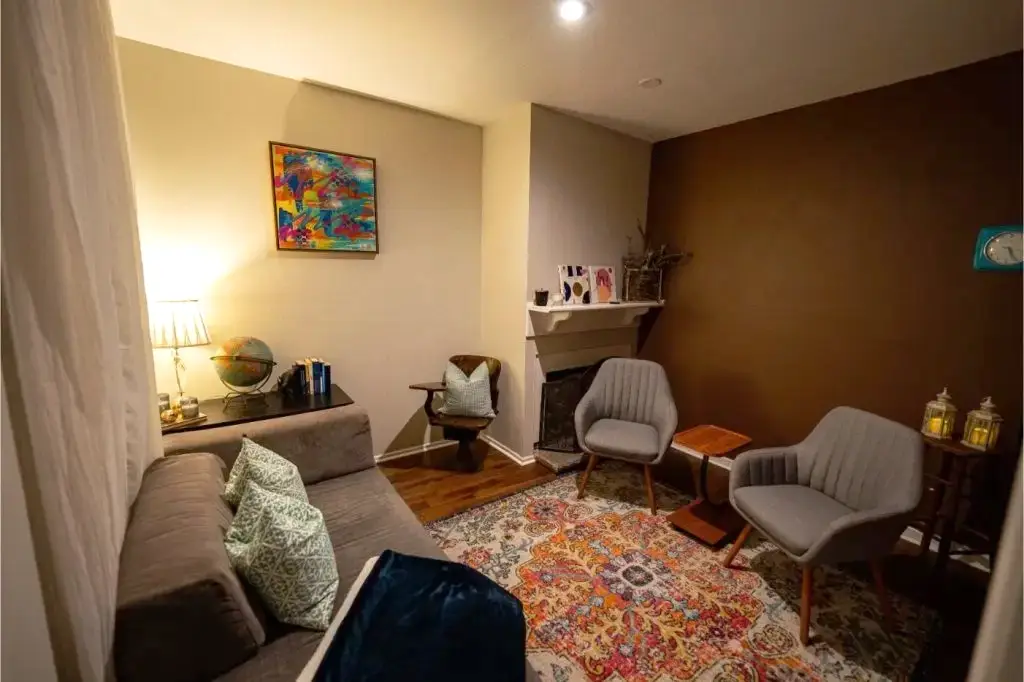 Therapy room with a gray couch, modern chairs, a fireplace, and soft lighting.